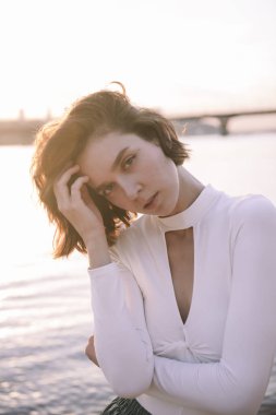 Gün batımında sahile yakın poz veren genç kadın portresi.