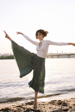 Güzel genç bir kadın poz veriyor ve günbatımı kumsalında yoga yapıyor.