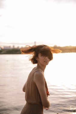 Mutlu genç bir kadın gün batımında gülümsüyor ve mutlu hissediyor.