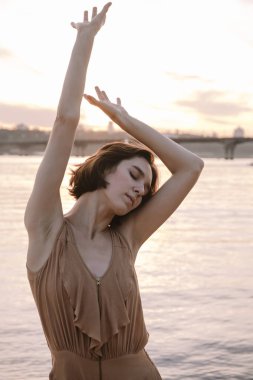 Gün batımında genç bir kadın poz veriyor ve yoga yapıyor.