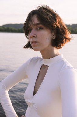 Gün batımında sahile yakın poz veren genç kadın portresi.