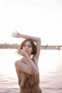 Gün batımında genç bir kadın poz veriyor ve yoga yapıyor.