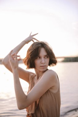 Gün batımında genç bir kadın poz veriyor ve yoga yapıyor.