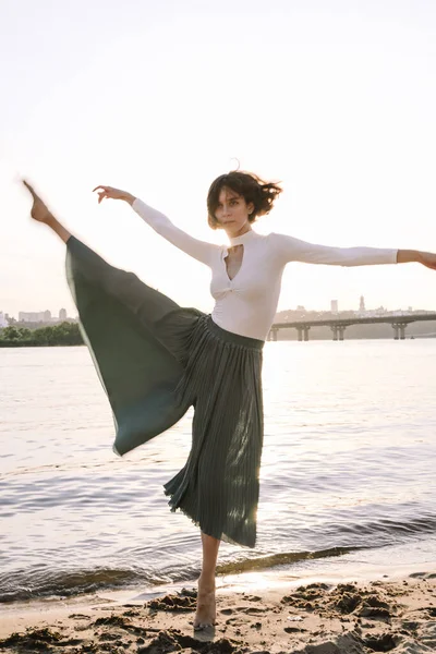 Güzel genç bir kadın poz veriyor ve günbatımı kumsalında yoga yapıyor.