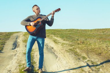 Genç bir adam gitar çalar. Yetenekli ellerde müzik aleti