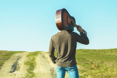 Omzunda gitar olan bir adam. Yolda dur.