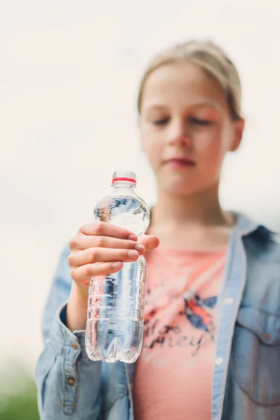 Девушка пьет воду на открытом воздухе - сосредоточьтесь на бутылке (только бутылка резкая) - очень мелкая глубина резкости — стоковое фото