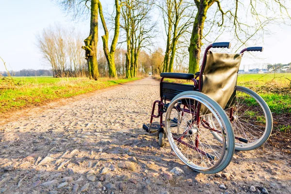 Пустое инвалидное кресло на полевой дороге на закате — стоковое фото