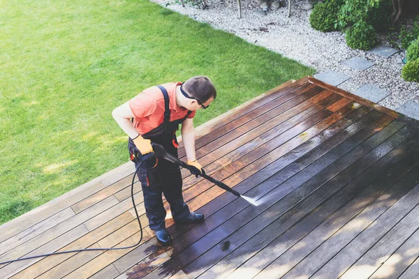 power washing - man cleaning terrace with a power washer - high water pressure cleaner on wooden terrace surface