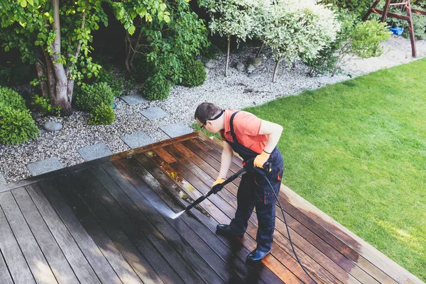power washing - man cleaning terrace with a power washer - high water pressure cleaner on wooden terrace surface