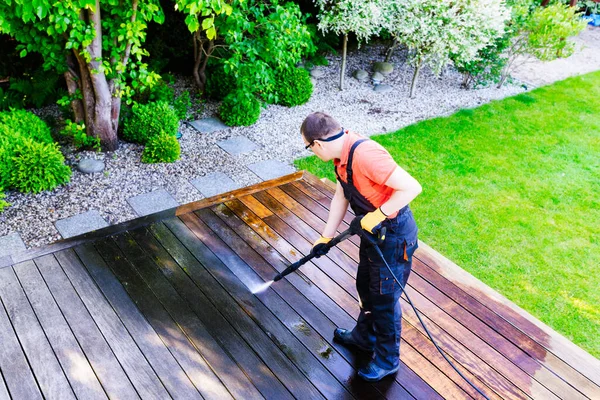 power washing - man worker cleaning terrace with a power washer - high water pressure cleaner on wooden terrace surface