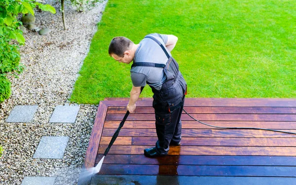 power washing - man worker cleaning terrace with a power washer - high water pressure cleaner on wooden terrace surface