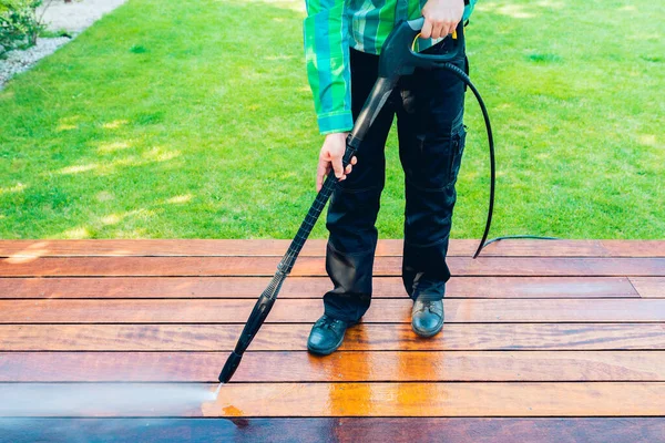 power washing - worker cleaning terrace with a power washer - high water pressure cleaner on wooden terrace surface