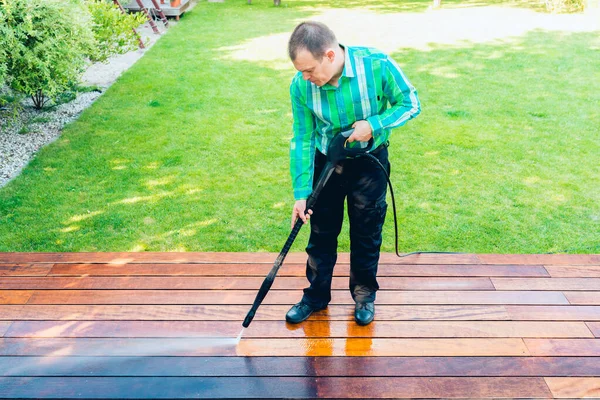 power washing - worker cleaning terrace with a power washer - high water pressure cleaner on wooden terrace surface