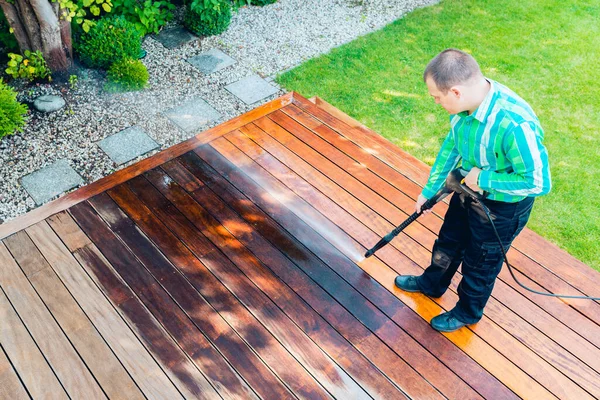 power washing - worker cleaning terrace with a power washer - high water pressure cleaner on wooden terrace surface