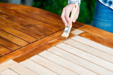 Terasta genç bir kız tarafından fırça ve yağlı bahçe masasının yenilenmesi