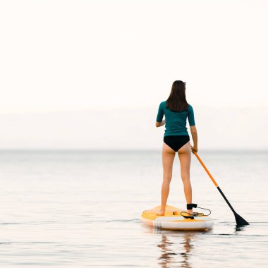 Elinde bir kürekle yemek masasında genç bir kız. Sırtından vurulmuş, denizin sakin yüzeyi, uzayı kopyalamış.