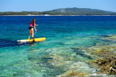 Elinde bir kürekle yemek masasında genç ve aktif bir kız. Sırtından vurulmuş, denizin sakin yüzeyi, uzayı kopyalamış.