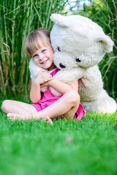 Little cute girl sitting in the grass with large teddy bear — Stock Photo, Image