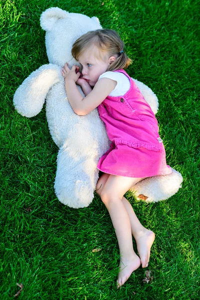 Сумна дівчинка лежить на траві з великим плюшевим ведмедем — стокове фото