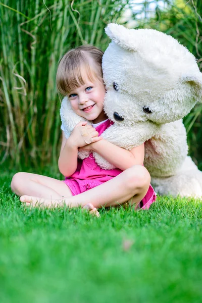 Little elfin girl sitting in the grass with large teddy bear — Stock Photo, Image