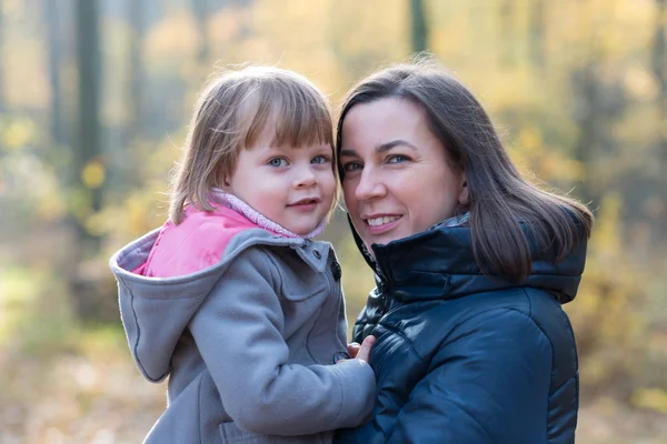 Mother holding daughter in autumnal forest smiling — Stock Photo, Image