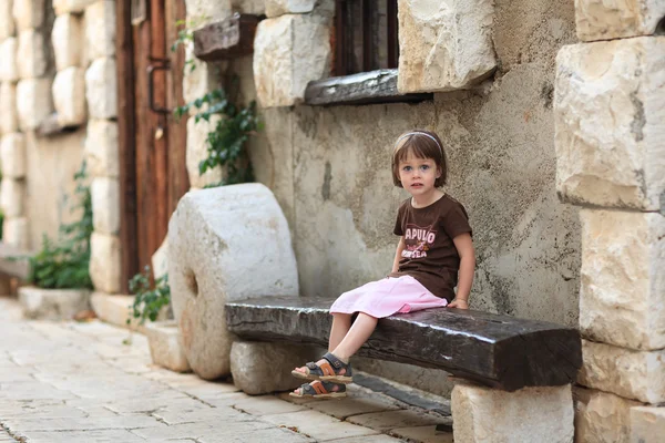 Eski bir ahşap bankta oturan küçük kız — Stok fotoğraf