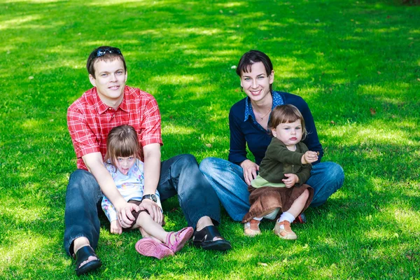 Happy family of four sitting on grass — Stock Photo, Image