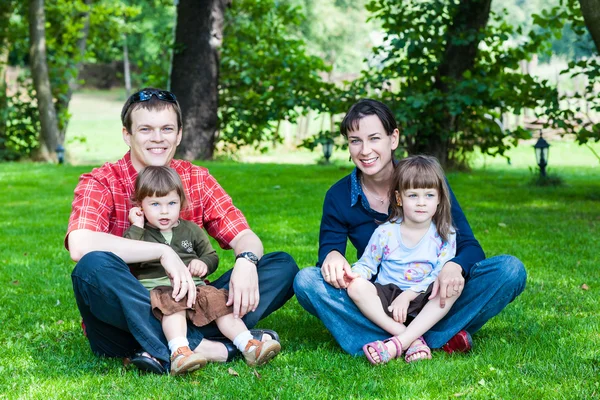 Happy family of four sitting on grass — Stock Photo, Image