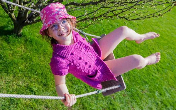 Счастливая девушка в розовой шляпе веселится на качелях на открытом воздухе — стоковое фото