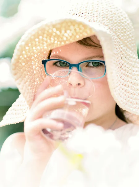 Sommar liten flicka i stråhatt dricksvatten utomhus porträtt. — Stockfoto