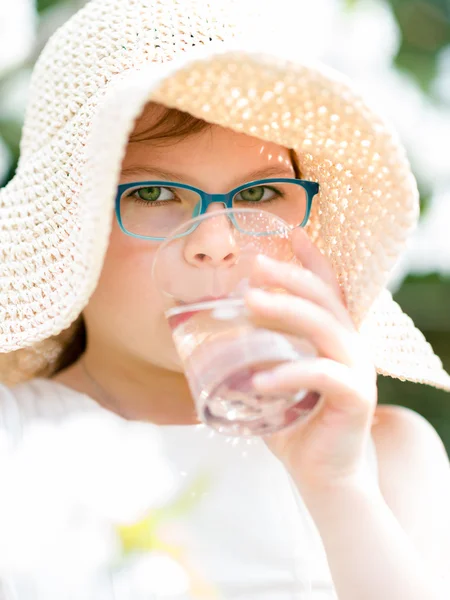 Sommar liten flicka i stråhatt dricksvatten utomhus porträtt. — Stockfoto