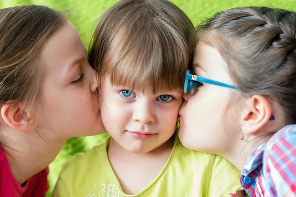 Surprised little girl kissed by two sisters. — Stock Photo, Image