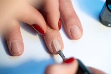 Profesyonel manikür, fırçayla çıplak jel cilası, arka planda zarif doğal tırnaklar ve kozmetik şişe, kuaförde ya da kaplıcada hassas güzellik tedavisi