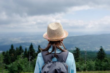 Sırt çantalı, hasır şapkalı ergen kız yürüyüşçü dağ manzarasına bakıyor, dramatik bulutlu gökyüzü altında fotokopi alanı olan dış mekan macera sahnesi..