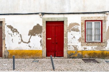 Portekiz cephesi koyu kırmızı kapılı ve uygun pencere çerçeveli, kaldırım taşı sokağının üzerindeki alçı ve elektrik kablolarını soyuyordu, kırsal mimari ve kentsel bozulma deseni detayı