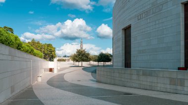 Modern kireçtaşı duvar ve dolambaçlı yol, Portekiz 'deki Fatima Tapınağı' ndaki Meryem Ana Bazilikası 'na doğru gidiyor. Bulutlu mavi bir gökyüzünün altında.