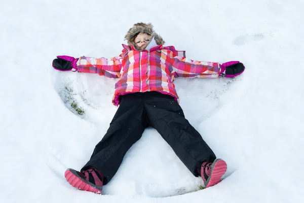 Malá holčička položila na sněhu a dělá angel — Stock fotografie
