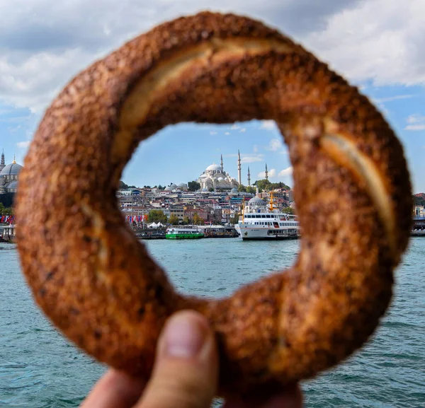 Традиционная турецкая выпечка - Simit в руке. Вид на старый город Стамбул и крупнейший город Турции. — стоковое фото