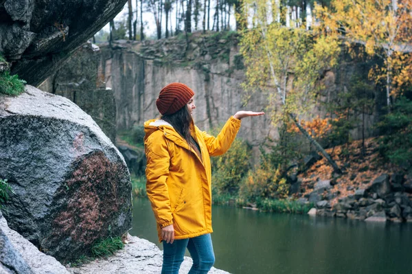 Mädchen in gelber Jacke und braunem Hut. Ein Spaziergang in den herbstlichen Bergen. Spaziergänger in den Felsen am Wasser in der Schlucht Korostyshiv. — Stockfoto