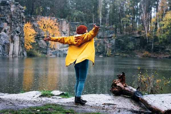 Mädchen in gelber Jacke und braunem Hut fängt Regentropfen in der Handfläche. Ein Spaziergang in den herbstlichen Bergen. Spaziergänger in den Felsen am Wasser in der Schlucht Korostyshiv. — Stockfoto