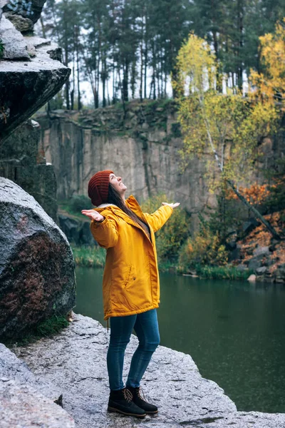 Mädchen in gelber Jacke und braunem Hut fängt Regentropfen in der Handfläche. Ein Spaziergang in den herbstlichen Bergen. Spaziergänger in den Felsen am Wasser in der Schlucht Korostyshiv. — Stockfoto