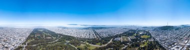 Golden Gate Parkı 'nın hava manzarası açık güneşli bir günde sağda ikiz tepeler ve ortada Presidio Parkı var. Golden Gate köprüsü bulutlarla kaplı.