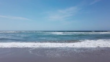 Kumlu sahilde mavi okyanus dalgaları ve açık mavi gökyüzü