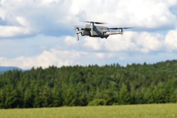 Uçan dron kuadkopteri orman ve tarla ile yan görüş alanında. Dijital kamerayla uçan İHA helikopter. Mavi gökyüzünde bir fotoğraf robotunun görüntüsü.