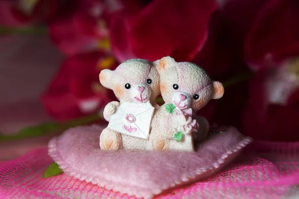 Sevgililer Günü için kalpleri ve çiçekleri olan pembe tekstil arka planında hatıra oyuncak ayılar.