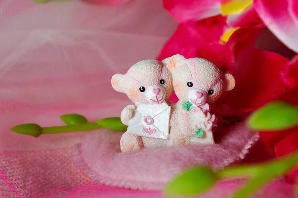 Sevgililer Günü için kalpleri ve çiçekleri olan pembe tekstil arka planında hatıra oyuncak ayılar.