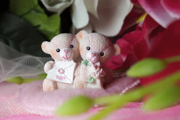 Sevgililer Günü için kalpleri ve çiçekleri olan pembe tekstil arka planında hatıra oyuncak ayılar.