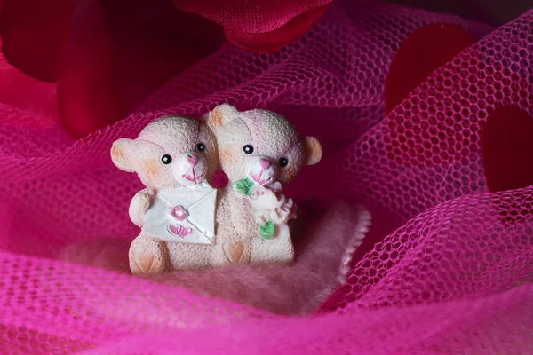 Sevgililer Günü için kalpleri ve çiçekleri olan pembe tekstil arka planında hatıra oyuncak ayılar.