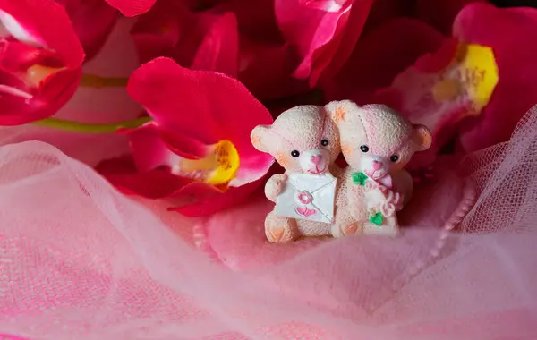 Sevgililer Günü için kalpleri ve çiçekleri olan pembe tekstil arka planında hatıra oyuncak ayılar.